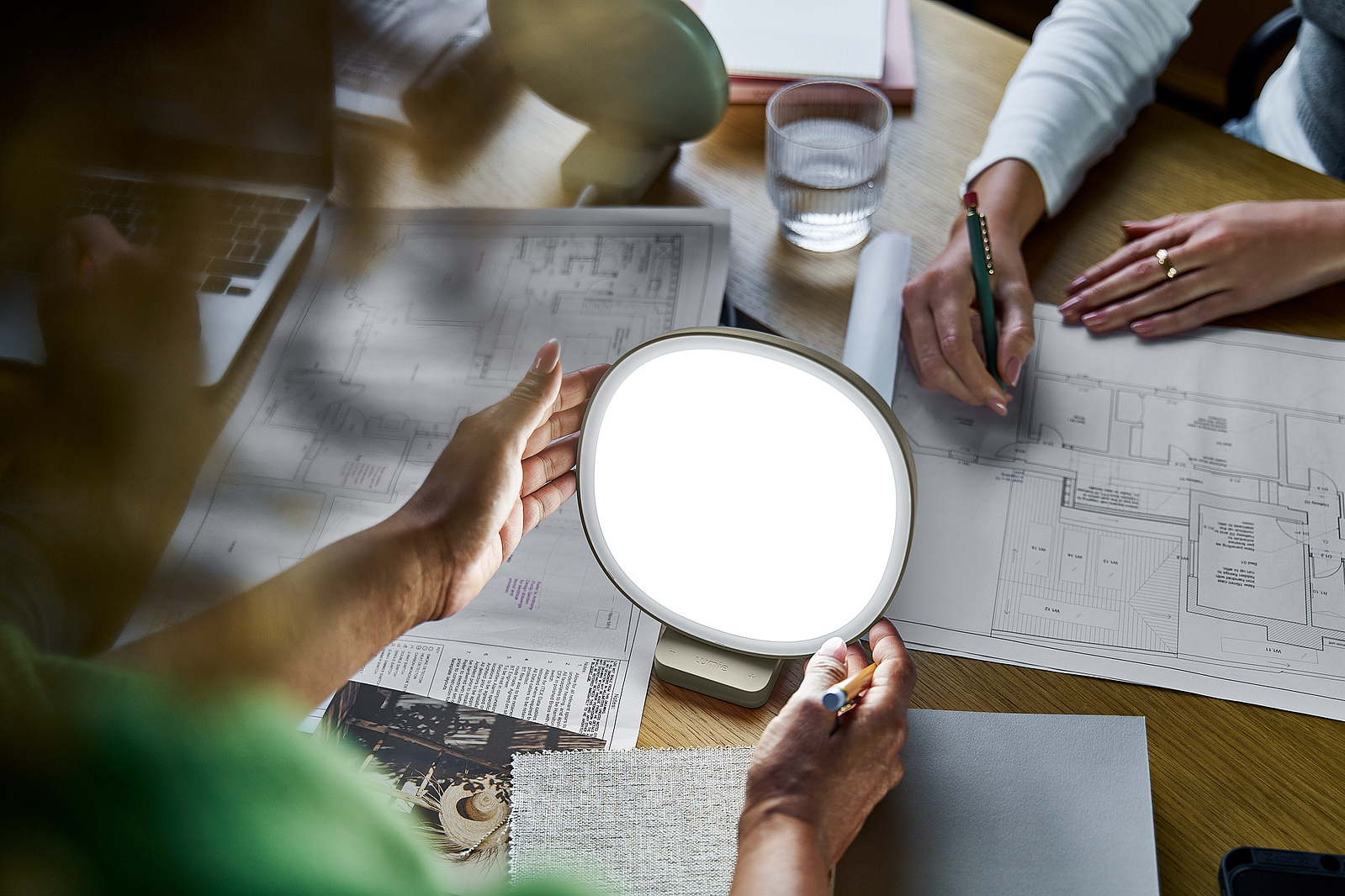 architects sit around a desk, adjusting a lamp. 