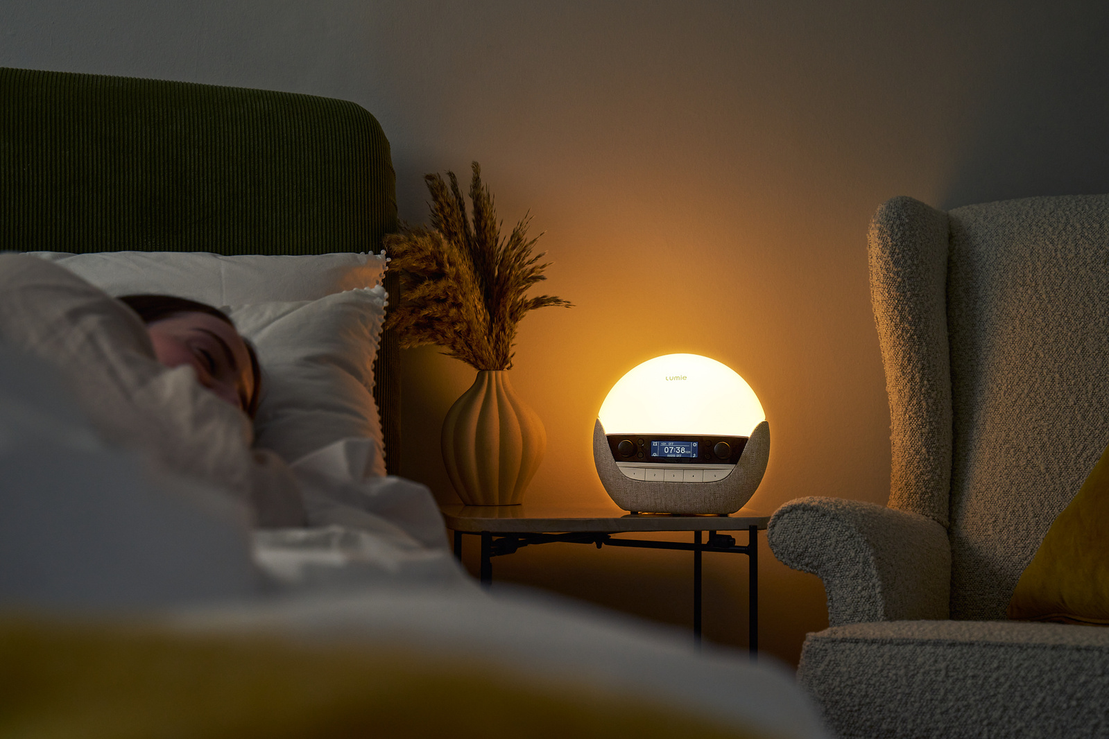 A woman is asleep in bed, illuminated by a soft warm glow of a bedside lamp. 