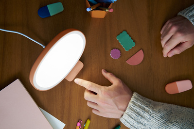 A top down photograph of a man adjusting a Lumie lamp amongst stationary. 