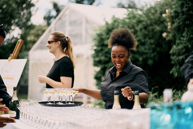 A happy black woman working onn an outside bar at an event. 