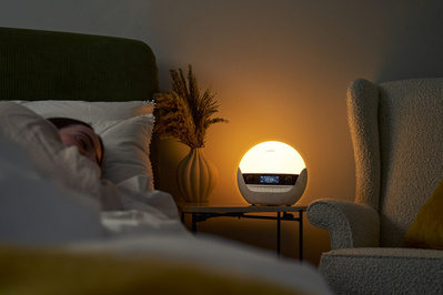 A woman is asleep in bed, illuminated by a soft warm glow of a bedside lamp. 