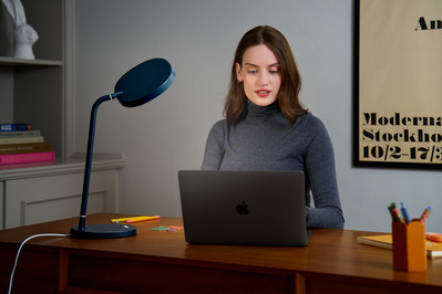 A woman working on her laptop in home office, illuminated by a tall lamp. 