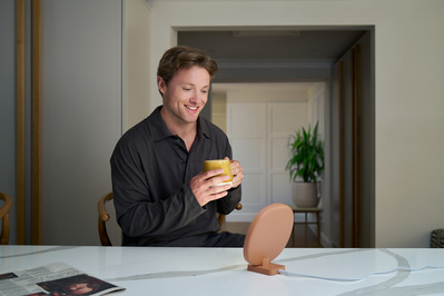 A man is sitting in the kitchen whilst drinking coffee. 