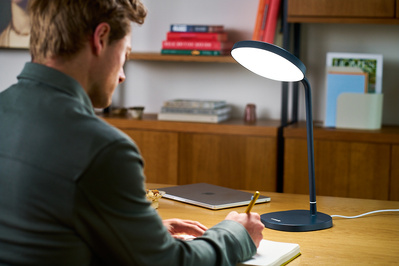 A man is working at a desk in a home office, illuminated by a lamp. 