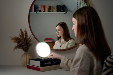 A woman sat in front of her large bedroom mirror, turning on her Lumie lamp. 