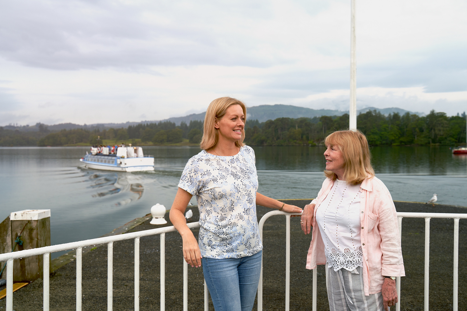 two people standing next to each other on a dock with a boat in the background
