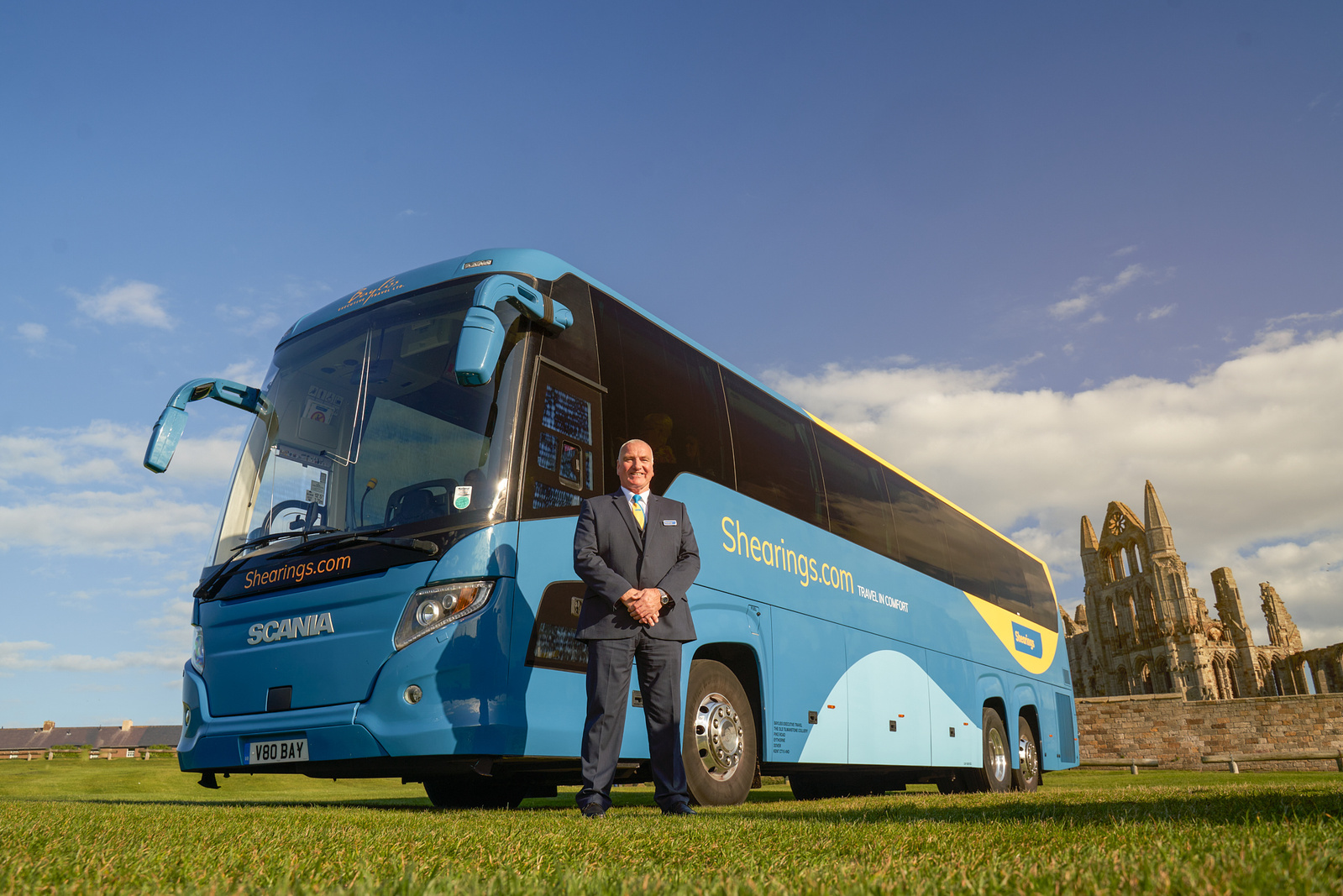 a person in a suit stands in front of a blue bus