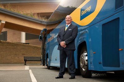 An Environmental portrait of a happy coach driver stood in front of his coach. 
