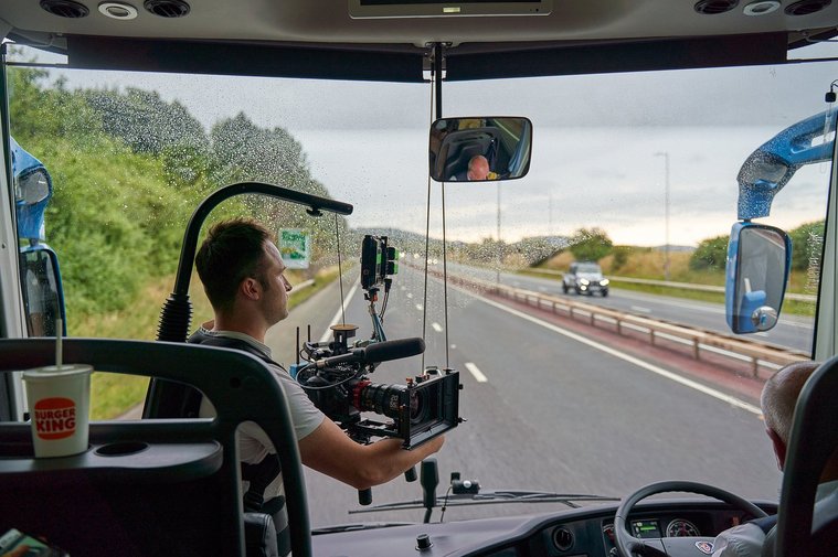 a person sitting in the driver's seat of a bus with a camera on their lap