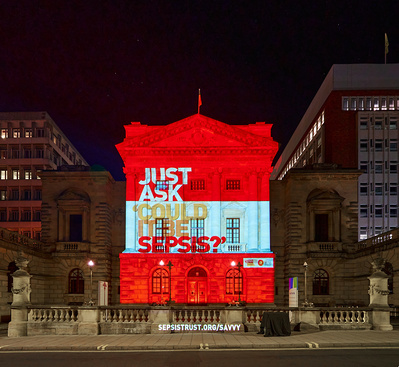 A grand building at night, illuminated by a colourful projection. 