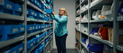 A woman stood between tall shelfs in a packaging facility. 