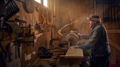 A man in his wood working workshop, lit by shafts of light coming through a window. 