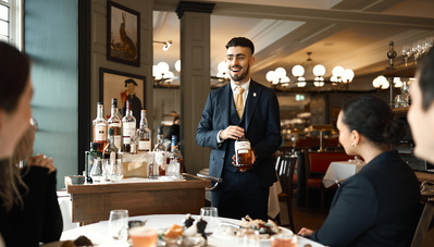 A restaurant sommelier stood at a table talking to guests in a restaurant. 