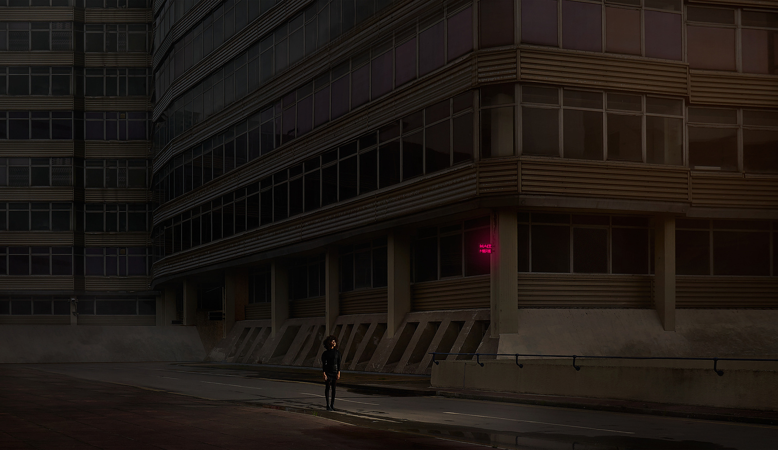 a person walking down the street in front of a tall building, illuminated by a neon sign. 