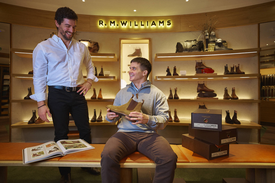 two people sitting on a bench in front of a shoe store