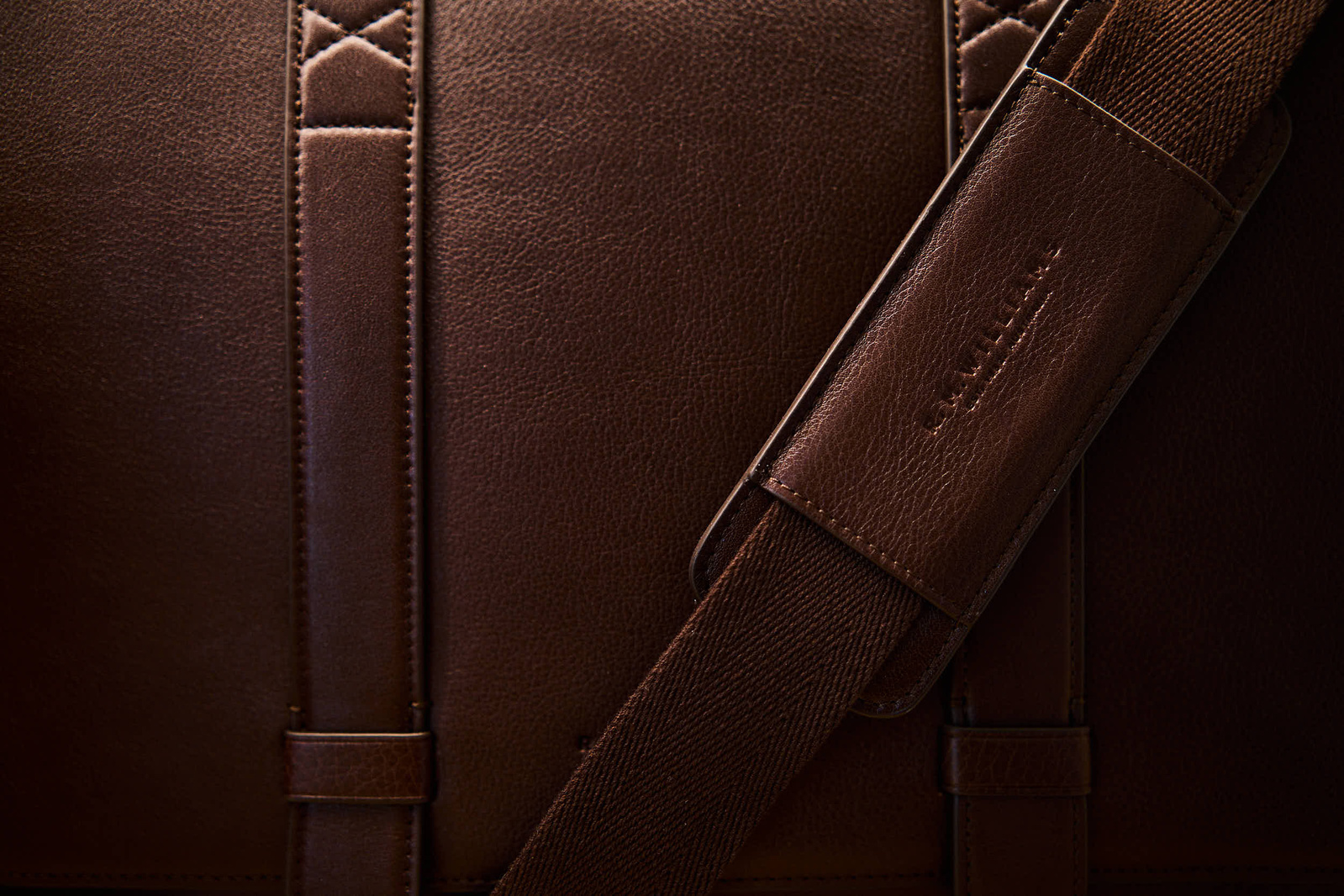 A cinematic close up still life shot of a mens brown leather satchel bag, completely filling the frame. 