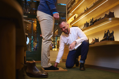 A man is being helped by a shop keeper in a shoe shop. 