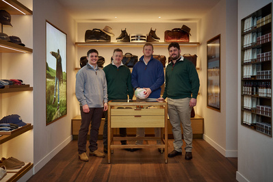 Four people standing in front of a display of shoes in a menswear shop. 