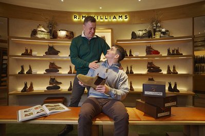 two people in a shoe shop in front of many pairs of shoes on shelves. 