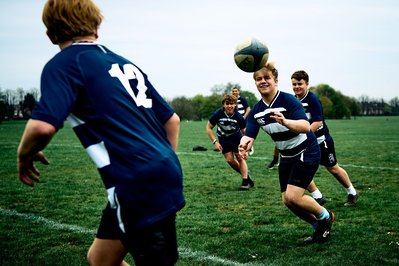 A group of boys are playing rugby and passing the ball down the formation line. 