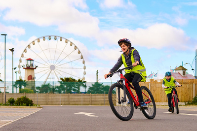Children cycling with a fair ground in the background. 