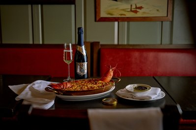 A moody restaurant setting where a lobster dish and a bottle of red wine is presented on the table. 