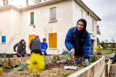 A young muslim girl is tending to a raised vegetable patch whilst her friends are gardening in the background. 