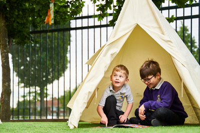Two young boys playing outside in a small tee-pee tent. 