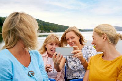 Four women take a selfie whilst sat on the top deck of a tourist ferry. 