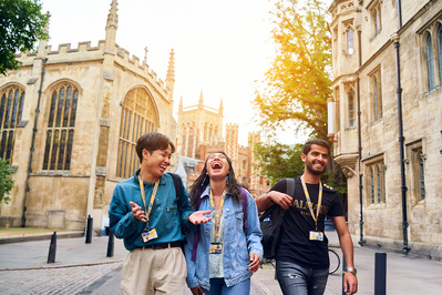 three happy university students walking hand in hand through the streets with the sun behind them. 