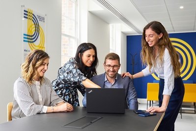 Four people gathered around a laptop in a modern office. 