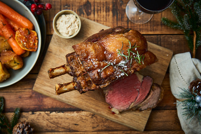 A top down photograph of a leg of lamb on a wooden chopping board. 