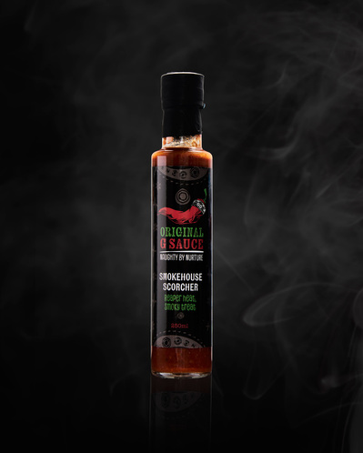 A product shot of a bottle of hot sauce, shot on a black background with smoke ehind the bottle. 