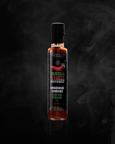 A product shot of a bottle of hot sauce, shot on a black background with smoke ehind the bottle. 