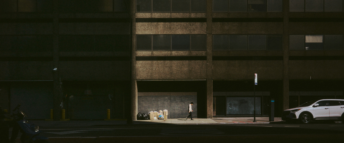 A man walks along a street illuminated by a low setting sun. 