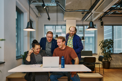 Four office workers gathered around a laptop computer and laughing in an office. 