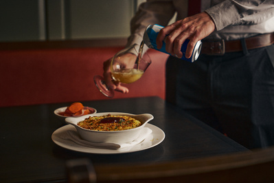 A close up of a waiter pouring a drink at a table in a restaurant. 