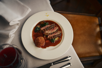 A top down photograph of a lamb dish in a restaurant with a glass of red wine on a white table cloth.  