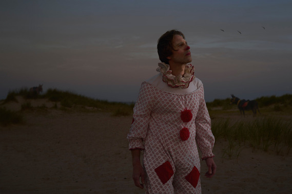 a person dressed as a clown stands on the beach