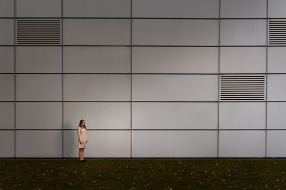 A woman stands very still against the avengers head office building, UEA. 