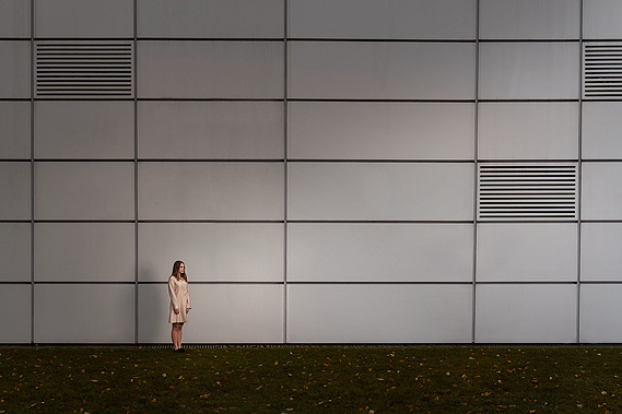 A woman stands very still against the avengers head office building, UEA. 
