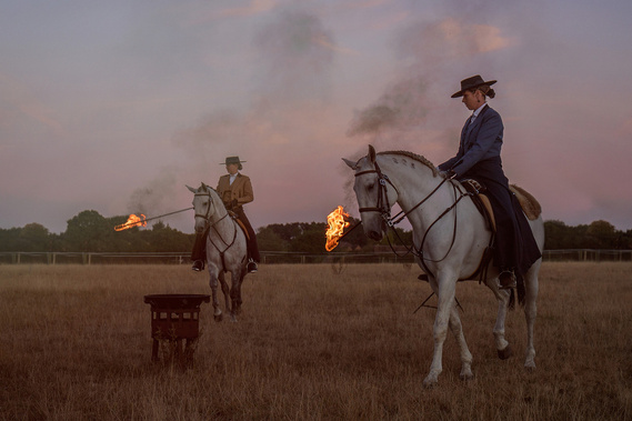 A cinematic and creative advertising photograph of horse riders in authentic Portuguese riding dress as they carry batons that are on fire. 