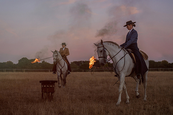 A cinematic and creative advertising photograph of horse riders in authentic Portuguese riding dress as they carry batons that are on fire. 