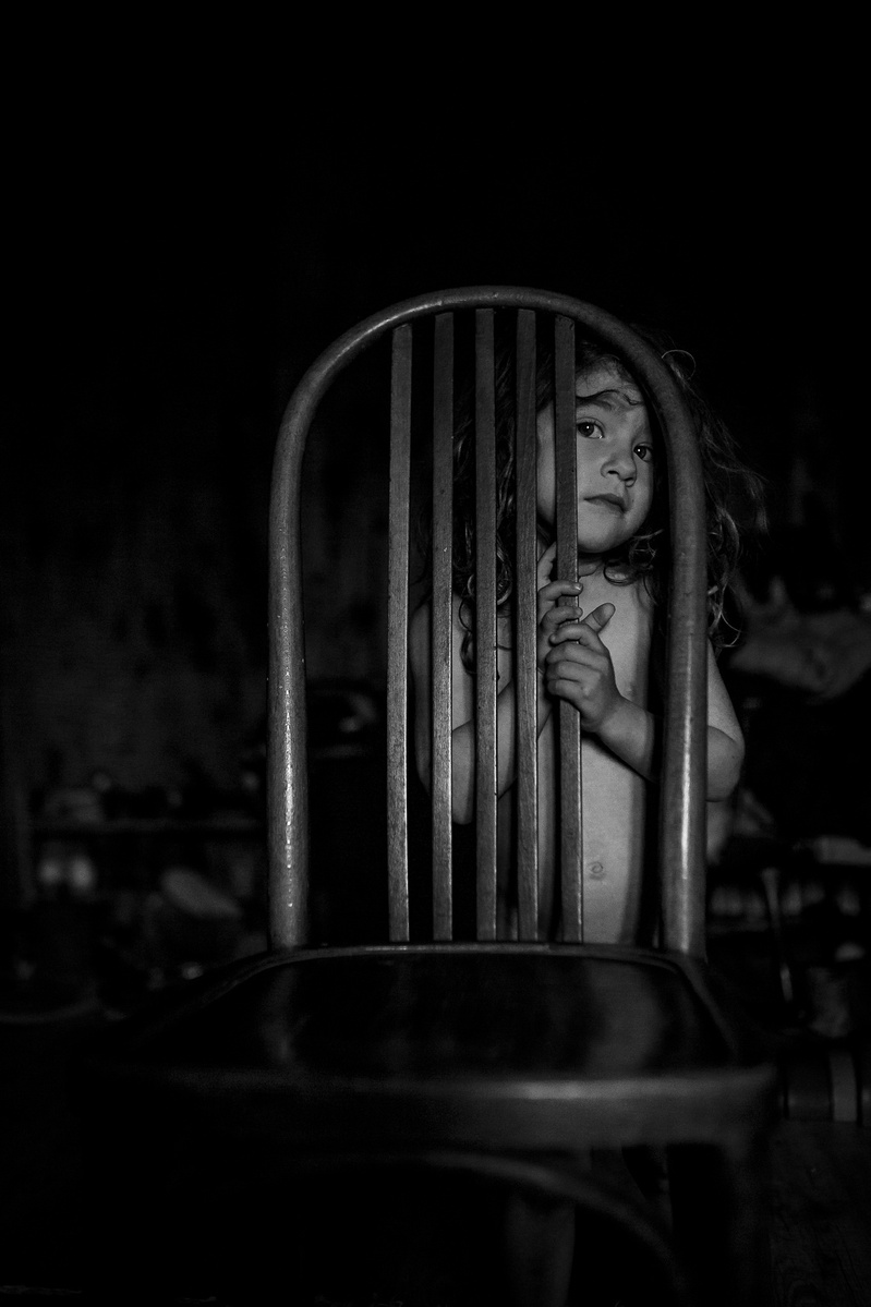 niña pequeña escondida detrás de los barrotes de una silla, en Olot, catalunya, españa 