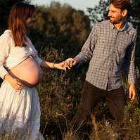 fotografía de una pareja paseando de la mano ella está embarazada  de 38 semanas, en los campos floridos de Pla de l'Estany, en girona, españa.