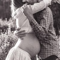 fotografía de una pareja abrazándoselo ella está embarazada  de 38 semanas, en los campos floridos de Pla de l'Estany, en girona, españa.