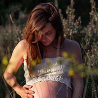 Mujer embarazada acaricia s vientre sentada en los prados del Plá de l'estany.
