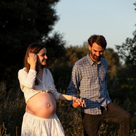 fotografía de una pareja paseando de la mano ella está embarazada  de 38 semanas, en los campos floridos de Pla de l'Estany, en girona, españa.