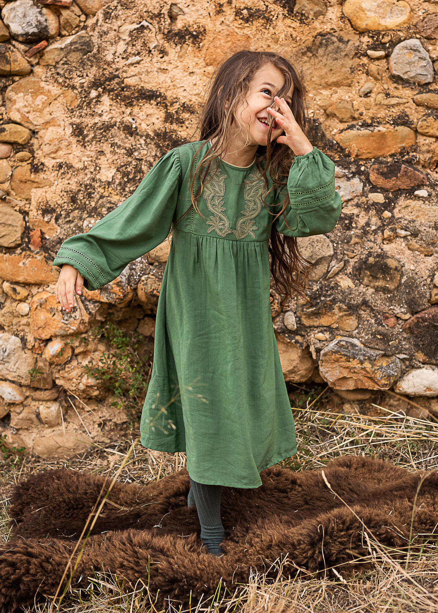 niña riendo delante de un muro de piedra de una Masia en Pla de l'Estany en cataluña, españa.