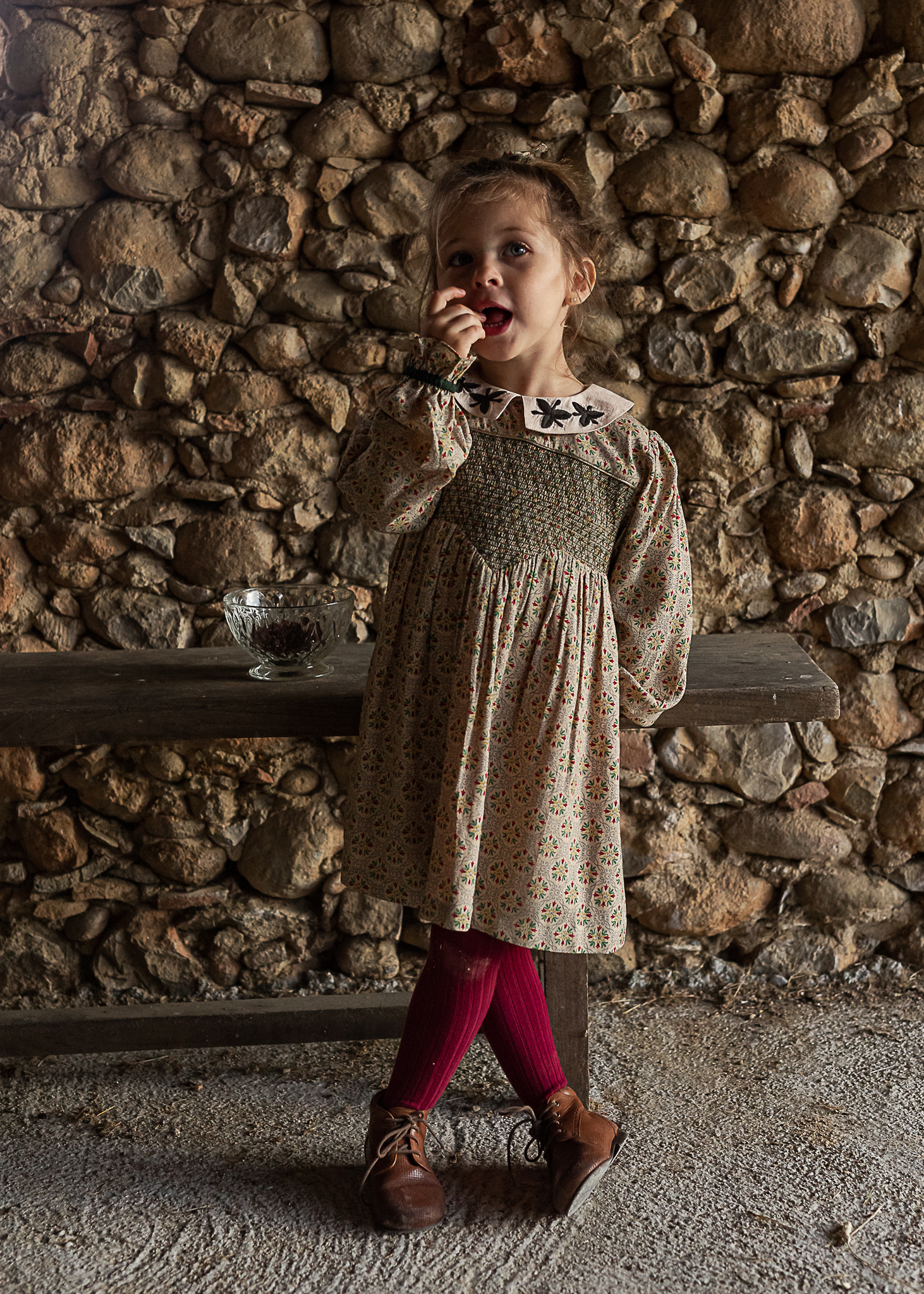 niña apoyada en un banco, comiendo pasas, en un pajar de una Masia en Pla de l'Estany, girona, españa
